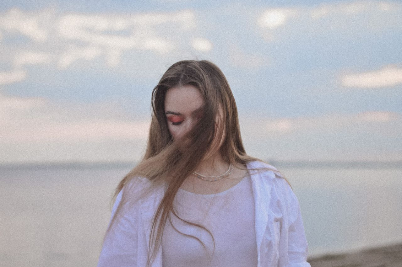 Vrouw staat aan zee met gesloten ogen en neemt bewust de ruimte om haar emoties te voelen.
