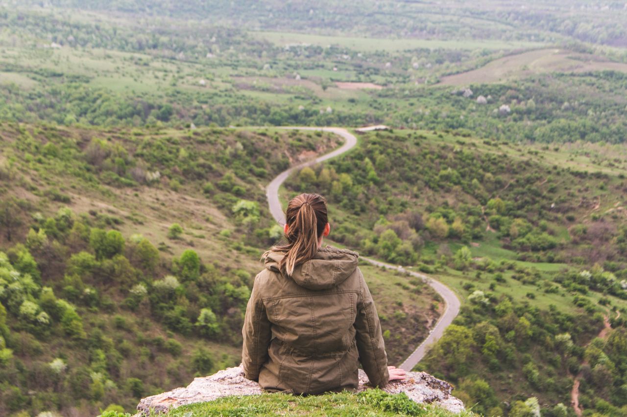 Een vrouw kijkt uit over het landschap met een zichtbaar pad als metafoor voor keuzes en richting.